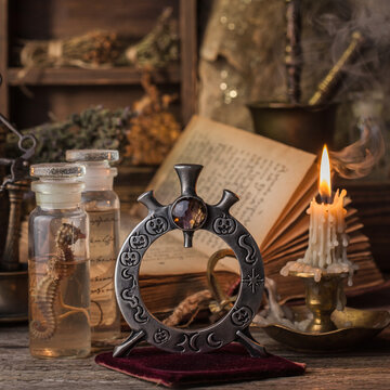 An atmospheric still life featuring an ornate metal ring, ancient books, glass bottles with mysterious liquids, dried herbs, and a flickering candle, evoking a sense of alchemy and mysticism.