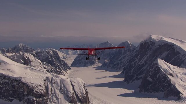 Red single propeller airplane flying above a vast, snow covered mountain range and glacier