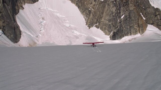 Red bush plane with skis landing on a vast, remote snow covered glacier surrounded by mountains