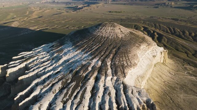 Aerial view from above and side of Mount Sherkala in the warm evening sunlight. Summer day, greening grass around the mountain amidst the desert zone of Mangystau. Wild nature, Martian landscapes