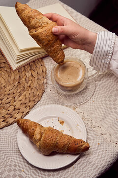 Hand dipping a croissant into a coffee cup with pastry on plate on a  linen tablecloth