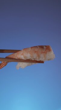 Wooden chopsticks holding fresh shrimp nigiri sushi moving into frame