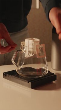Vertical POV of barista preparing drip coffee bag on glass server