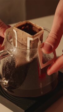 Removing used drip coffee bag from glass server vertical POV