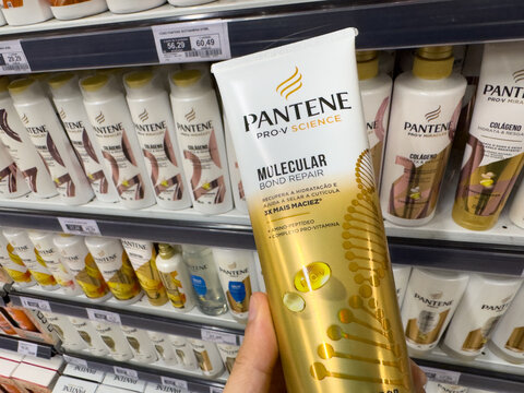 BELO HORIZONTE, MG, BRAZIL, MAY, 15, 2026 A hand holding a tube of Pantene Pro-V Science Molecular hair care product in front of a store shelf stocked with various Pantene products
