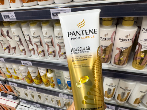 BELO HORIZONTE, MG, BRAZIL, MAY, 15, 2026 A hand holding a tube of Pantene Pro-V Science Molecular Repair hair conditioner in front of a store shelf stocked with various Pantene products