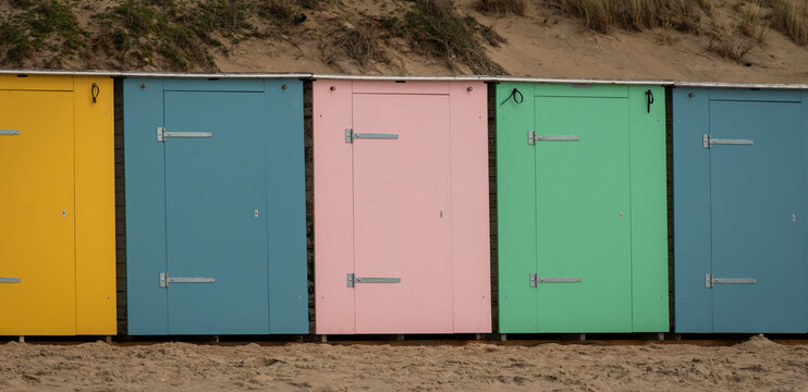 row of pastel colored coastal beach cabines near ocean and dunes
