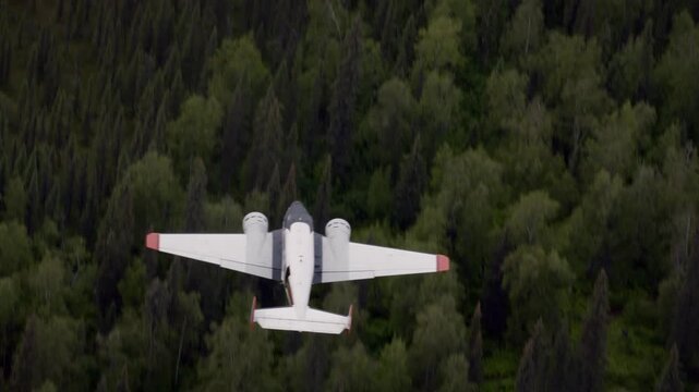 Twin engine propeller seaplane flying over a wild and dense green forest in Alaska