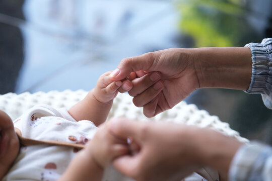 closeup of mother's fingers and baby's hand holding each other. A mother plays with her baby. their hands held each other gently. Immortalize love, protection and new life in a loving embrace.
