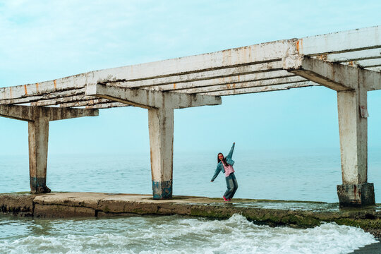 Girl dancing on a ruined concrete pier by the sea in summer