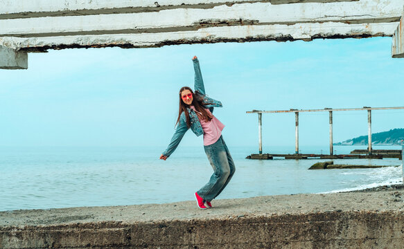 Dancing girl in denim on a concrete pier by the sea in summer