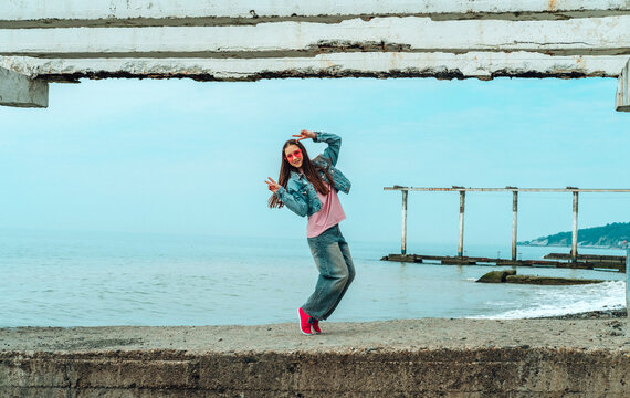 Dancing girl in denim on a concrete pier by the sea in summer