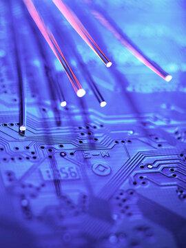 Glowing fibre optic cables over blue computer circuit board