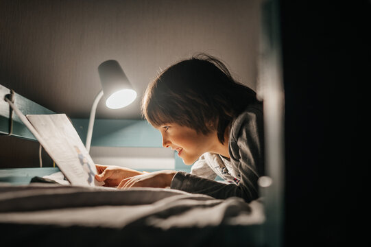 Child reading a book in bed under lamp light at night