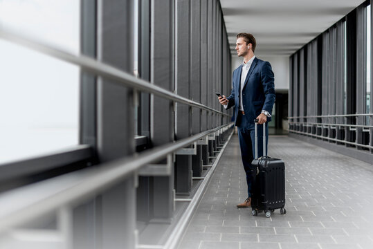 Business executive with suitcase looking out window at airport