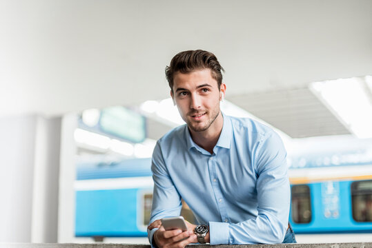 Smiling business professional holding cell phone at train station