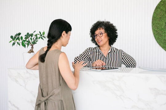 Woman at reception counter talking to receptionist using digital tablet