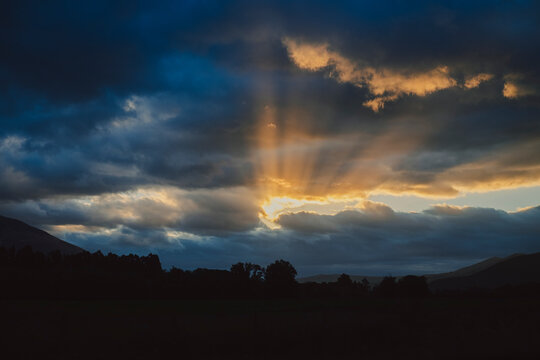 Dramatic sunset with sunbeams over a New Zealand mountain landscape