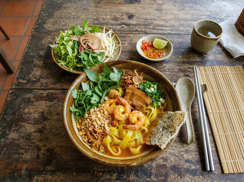 Vietnamese Mi Quang noodle dish with shrimp and herbs on rustic table