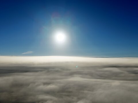 defaultFotografia a&eacute;rea capturada por drone mostrando um mar de nuvens brancas sob um c&eacute;u azul limpo com o sol brilhando intensamente ao centro. Ideal para conceitos de liberdade,  viagens e natureza.