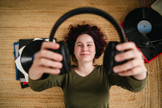 Smiling music fan holding headphones near turntable on rug