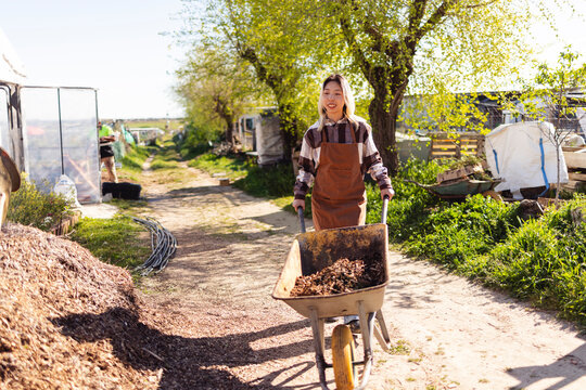 Farmer pushing wheelbarrow with compost outdoors on a farmstead