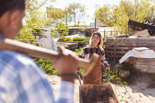 Gardeners pushing wheelbarrow with compost at sunny farmstead