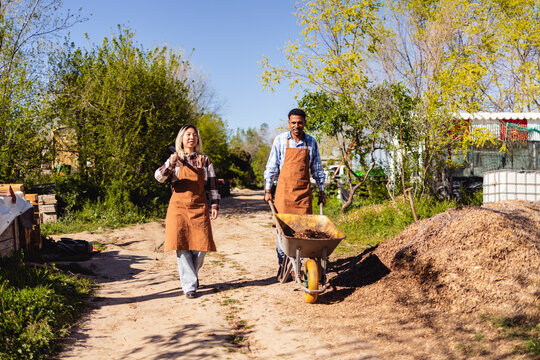 Smiling farmers walking with wheelbarrow in community garden