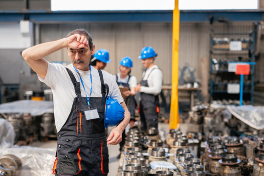 Exhausted worker wiping sweat at indoor manufacturing factory