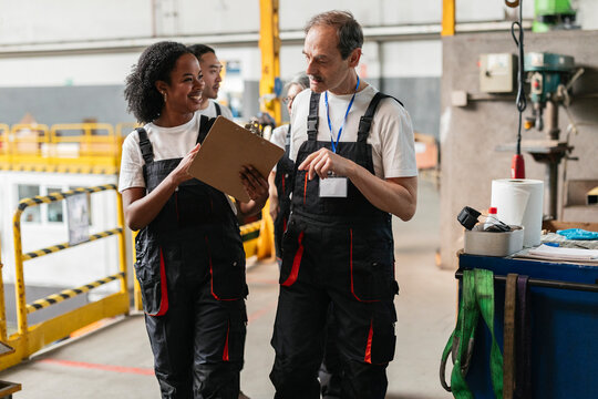 Technician and colleague discuss maintenance on clipboard in factory