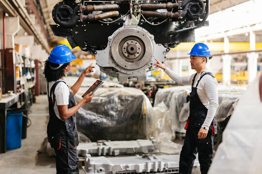 Engineers inspecting heavy machinery with tablet in factory