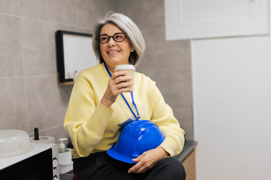 Smiling architect holding a coffee cup and helmet in an office