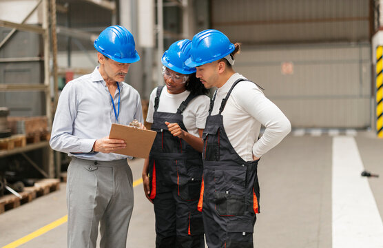 Manager and engineers discuss checklist on clipboard in factory