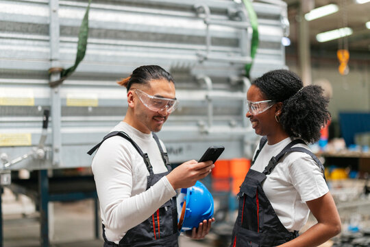 Two industrial workers smiling and looking at a smartphone in a factory