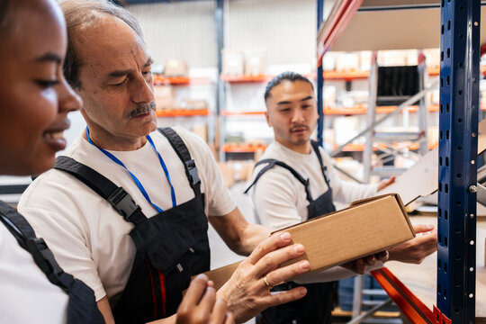 Warehouse workers examining cardboard box indoors