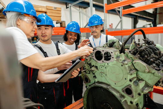 Engineering team inspecting heavy machinery with tablet indoors
