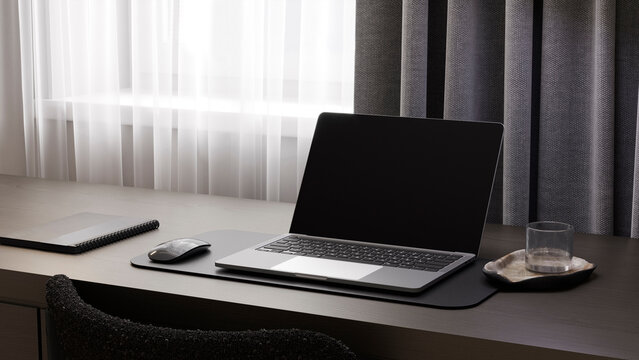 Blank laptop screen mockup on a dark desk indoors