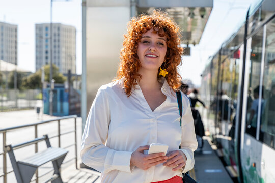 Smiling commuter using smartphone at a tram station in Granada