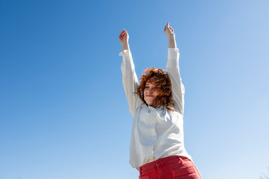 Smiling person with arms raised under a blue sky in Granada Spain