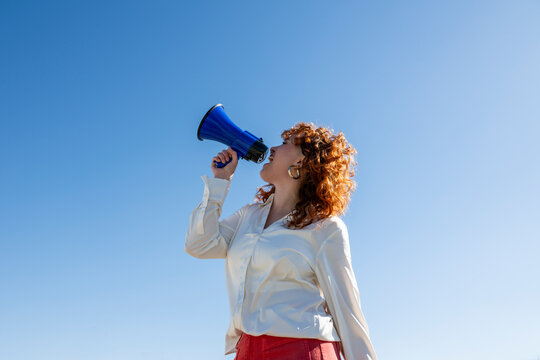 Holding a blue megaphone and shouting against a clear blue sky