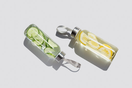 Tasty Water drink detox in bottles on white table, hard shadow at sunlight. Self care, wellness, diet, healthy living concept. Glass reusable water bottle, eco friendly still life minimal aesthetics.