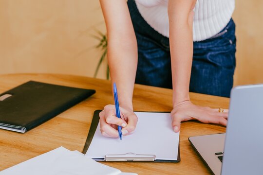 Manager leaning on wooden office desk writing on clipboard