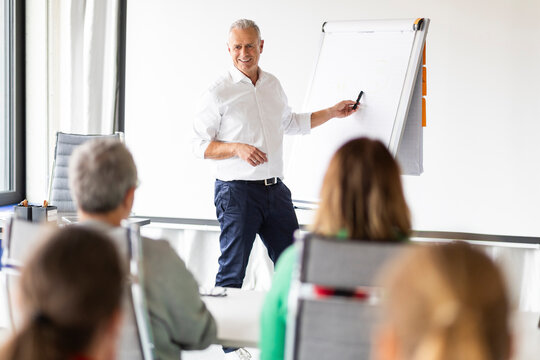 Happy businessman explaining strategies on whiteboard at office workshop