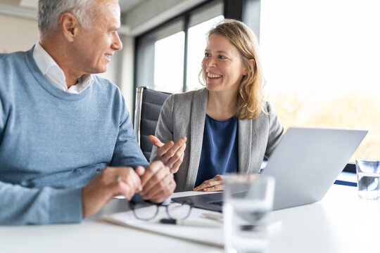 Mature businesswoman sitting and talking with colleague in office