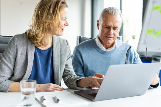 Smiling businesswoman discussing on laptop with colleague sitting in office