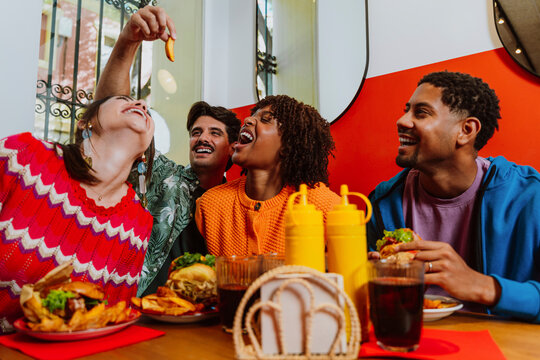 Happy friends laughing and eating burgers in a restaurant