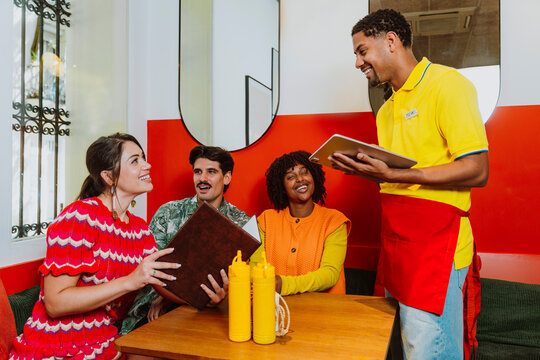 Smiling waiter taking order from friends at a restaurant table