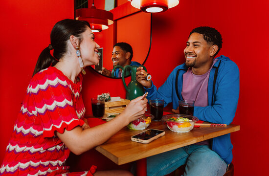 Smiling couple eating sushi on a dinner date at a red restaurant