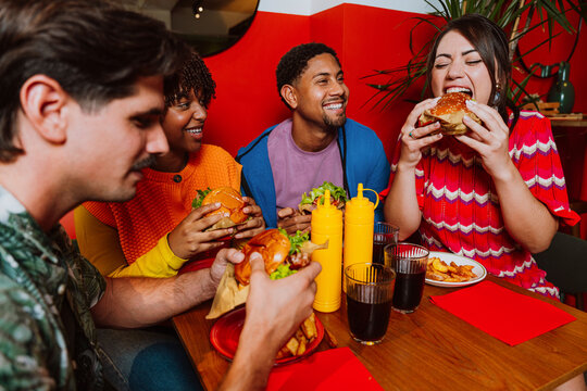Friends eating burgers and laughing together at a restaurant indoors