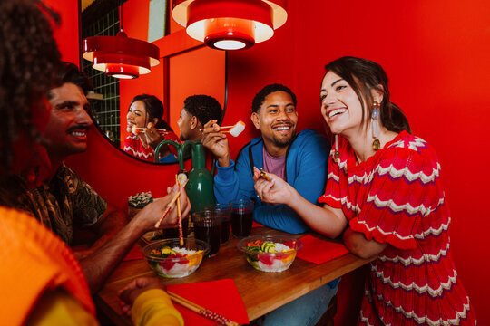 Friends eating sushi and laughing at a bright red restaurant